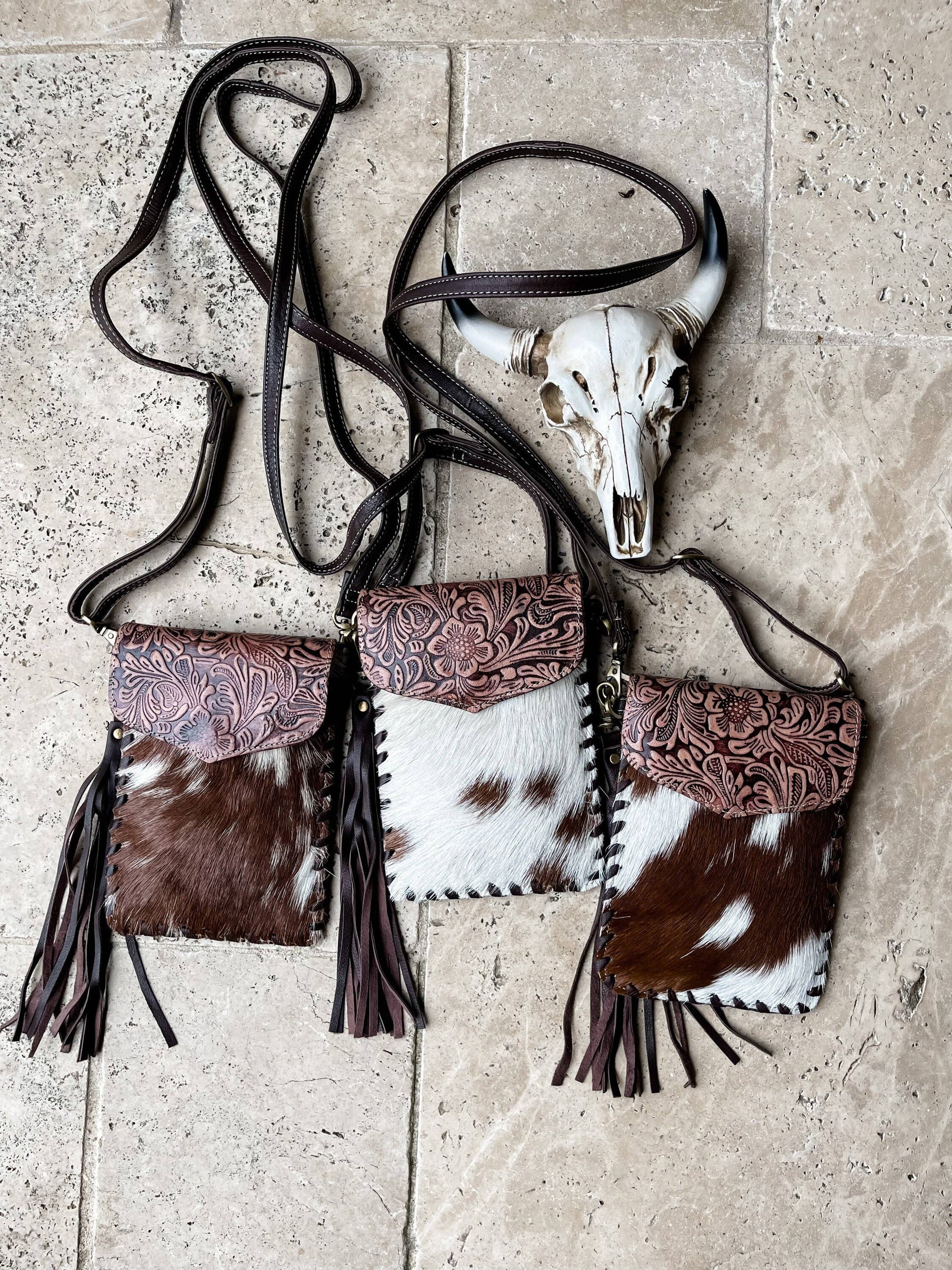 Cowhide leather handbag with tassels and a cow skull on a stone surface