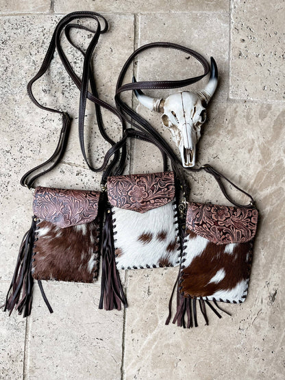 Cowhide leather handbag with tassels and a cow skull on a stone surface