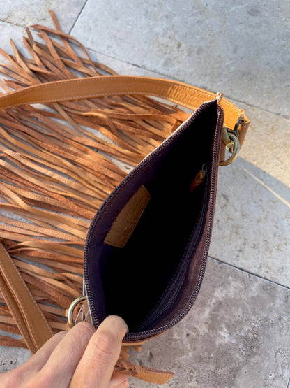 Brown leather handbag with fringe details on a concrete surface