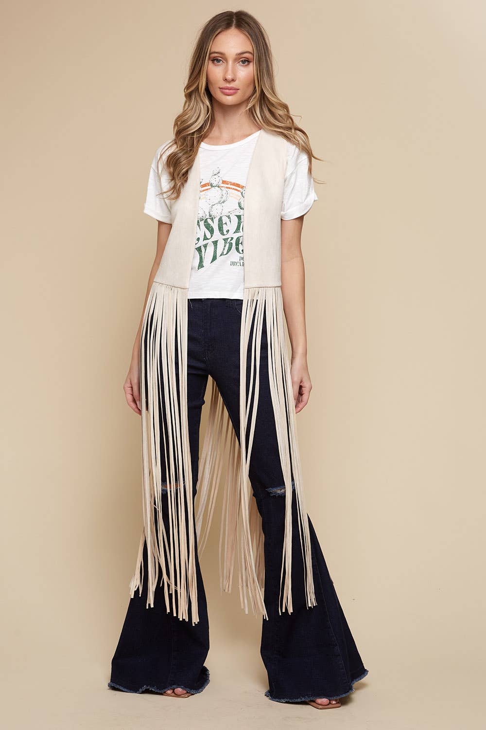 Woman wearing a white t-shirt with text and fringed black pants on a beige background