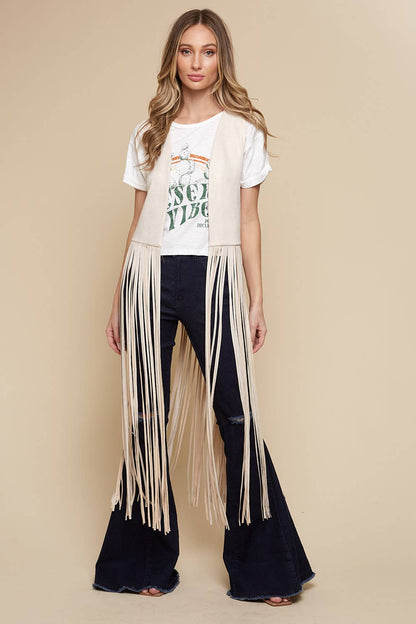 Woman wearing a white t-shirt with text and fringed black pants on a beige background