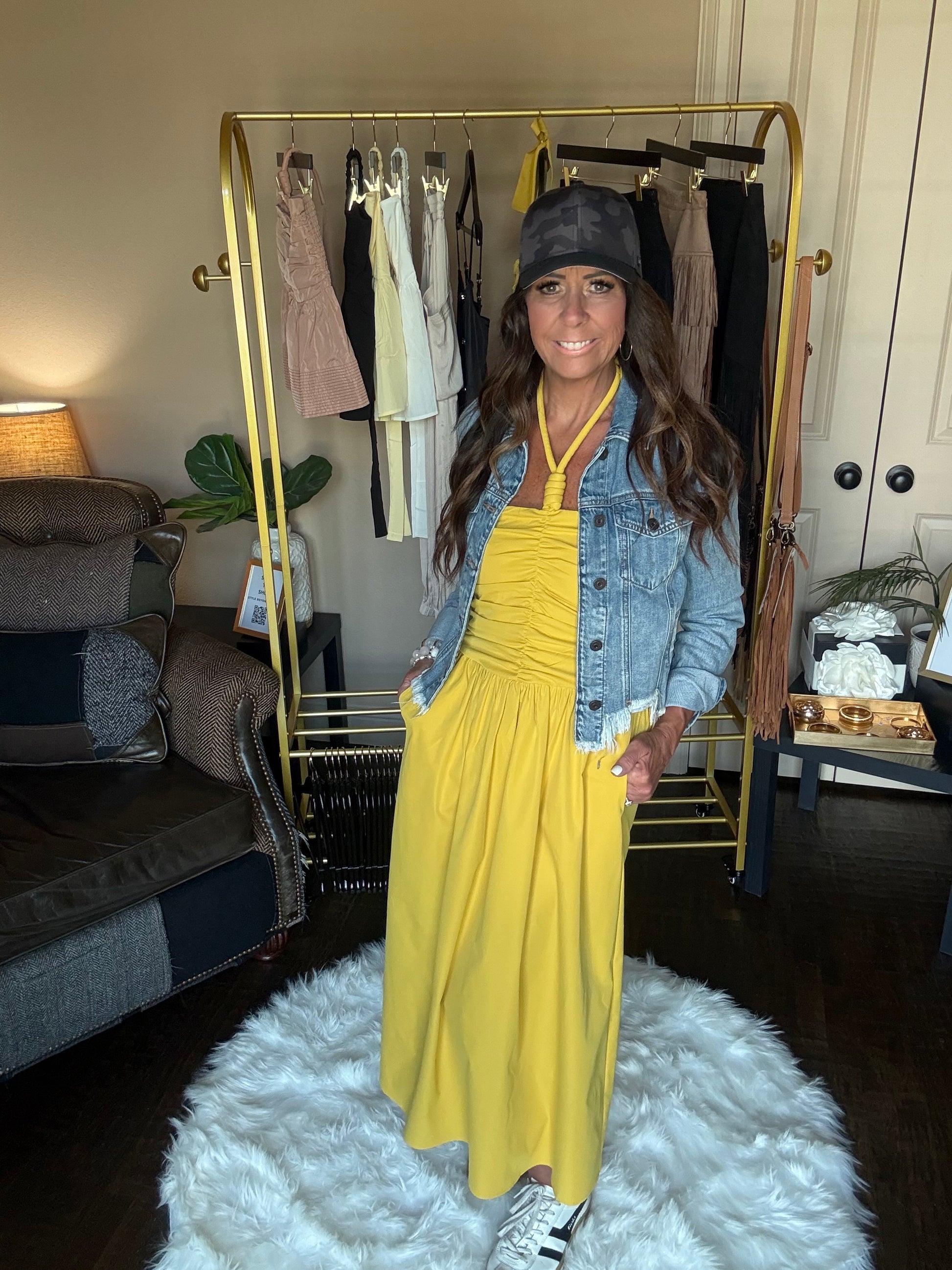 Woman wearing a yellow dress and denim jacket in a room with a gold bar cart and white rug.
