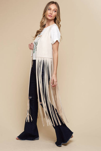 Woman wearing a white top with fringe and black pants on a beige background