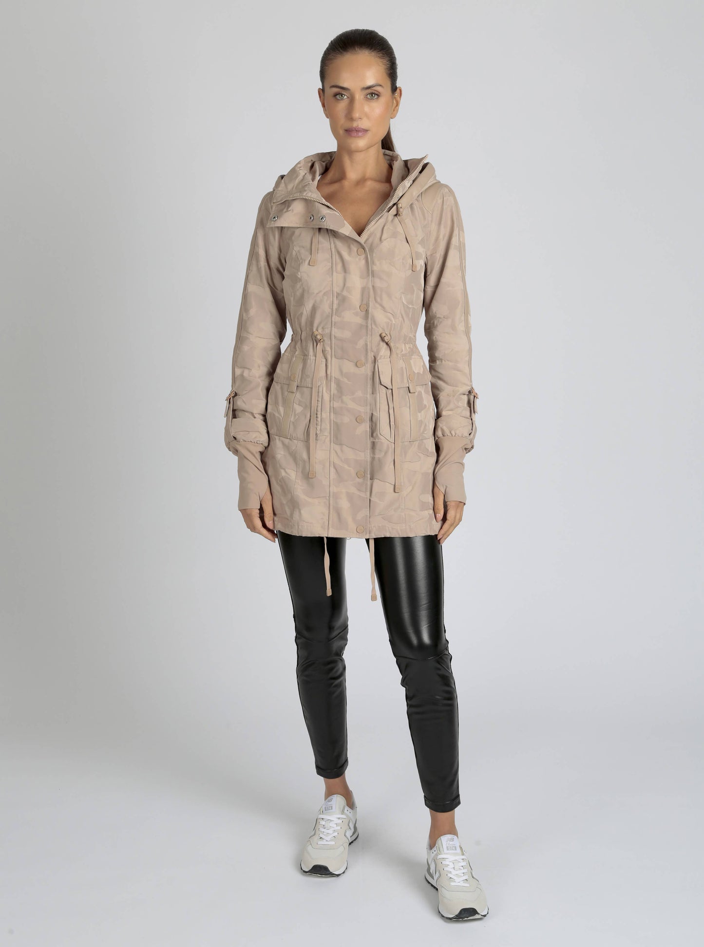 Woman wearing a beige hooded jacket and black leather pants on a white background