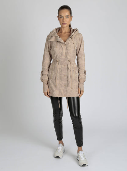 Woman wearing a beige hooded jacket and black leather pants on a white background