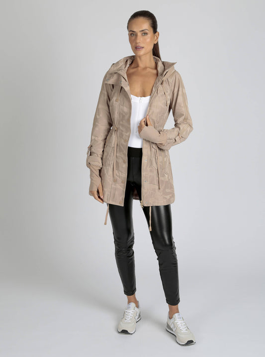 Woman wearing a beige trench coat over a white top and black pants on a light gray background