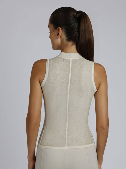 Woman wearing a beige sleeveless top against a plain background
