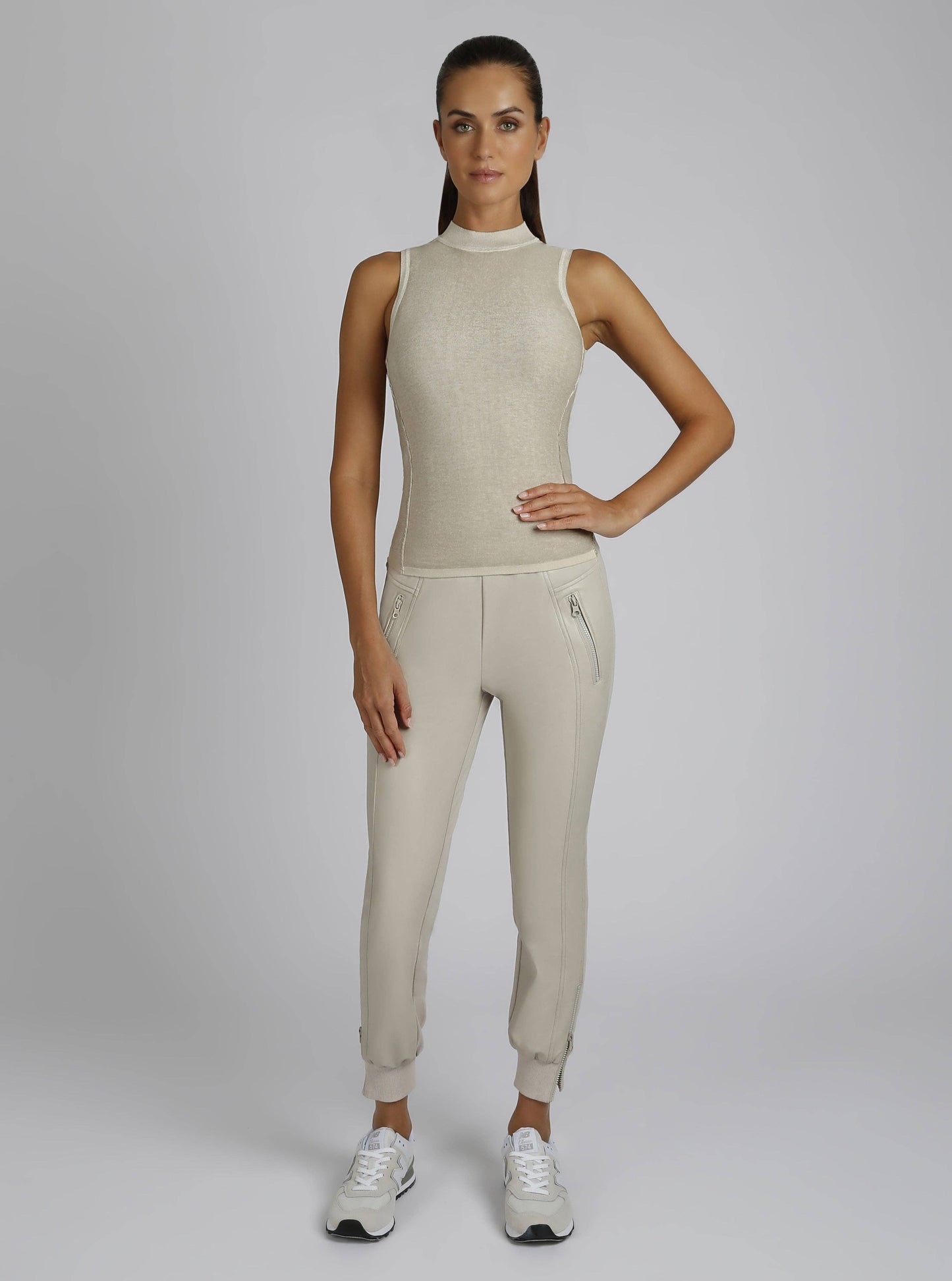 Woman wearing a beige sleeveless top and jogger pants on a white background