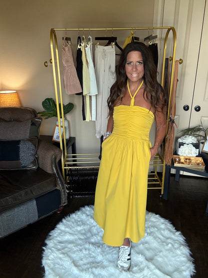 Woman in a yellow dress standing in a room with furniture and decor.