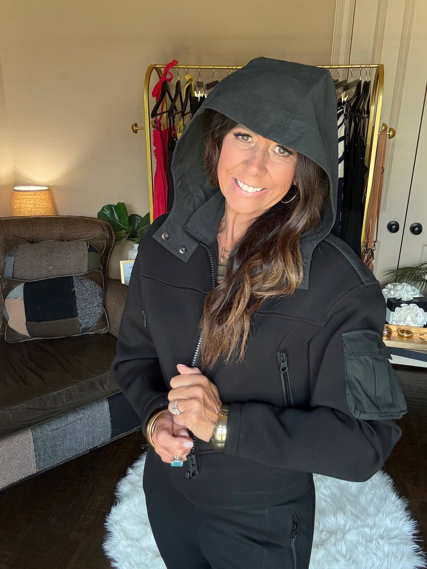 Woman in a black coat holding a suitcase in a room with a lamp and plant.
