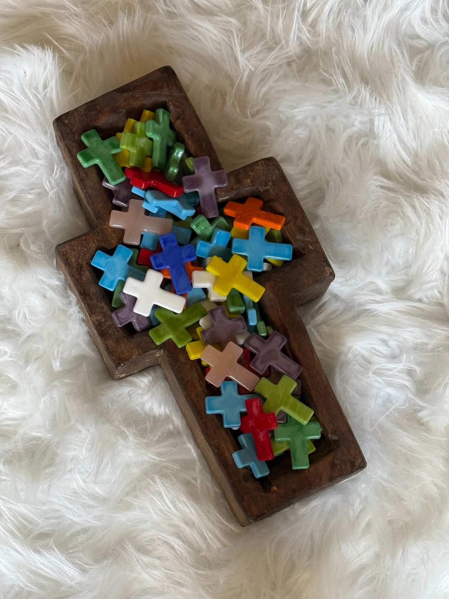 Wooden cross with colorful glass crosses on a white fluffy surface.