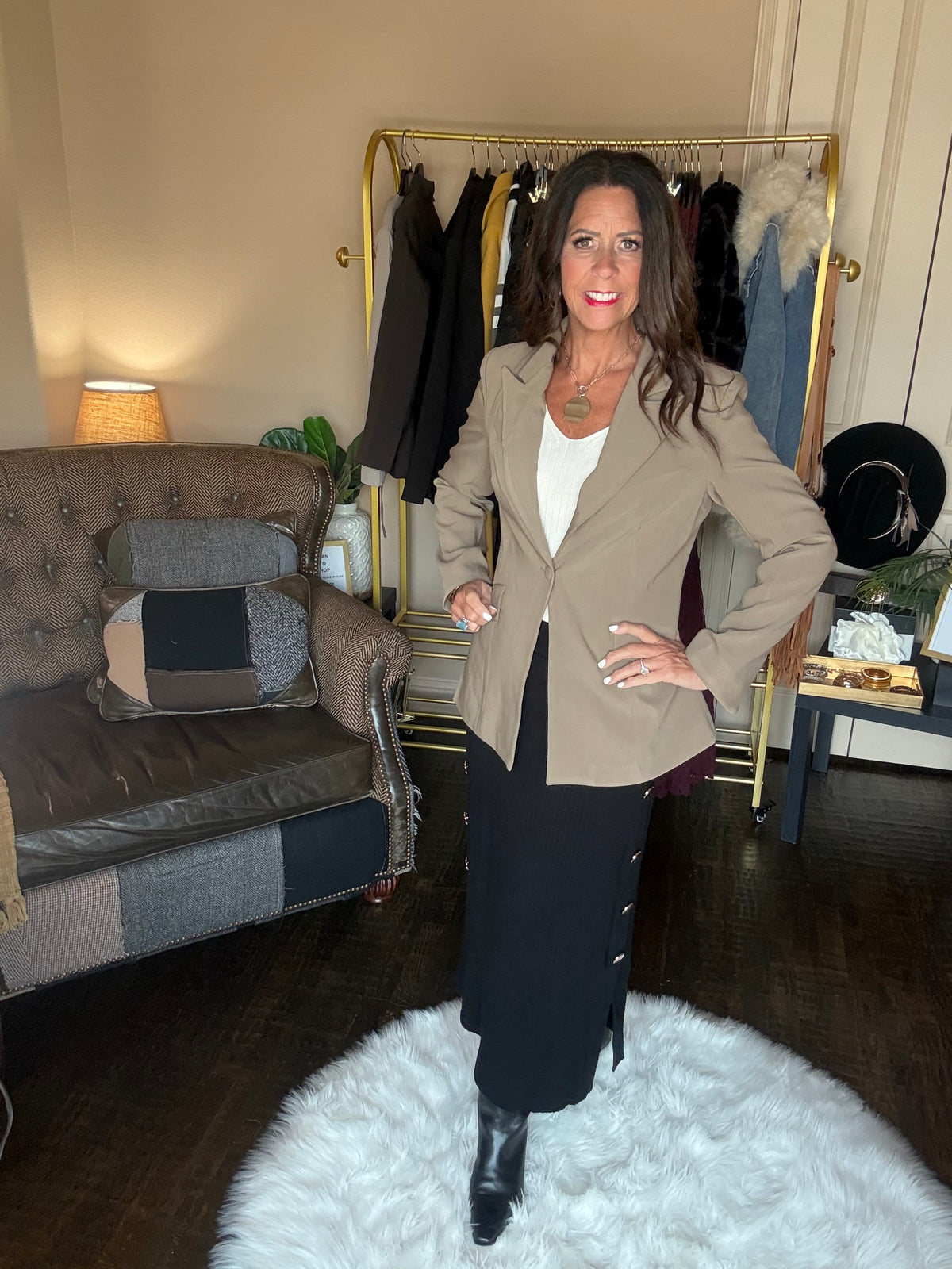 Model is wearing a khaki blazer with a cream top, black ribbed maxi skirt with gold button details, and black booties
