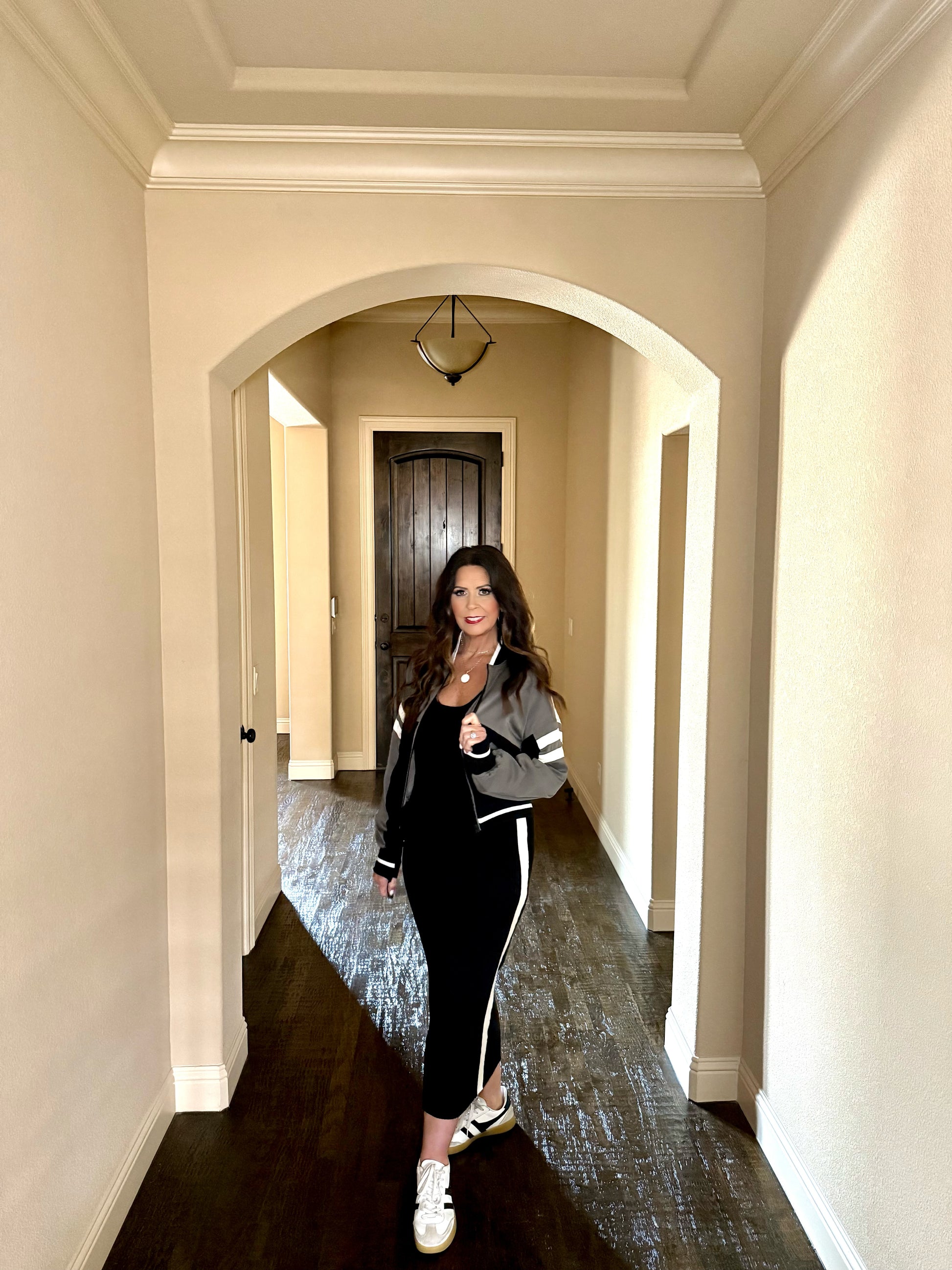Woman in a black and white outfit standing in a hallway with arched doorways.