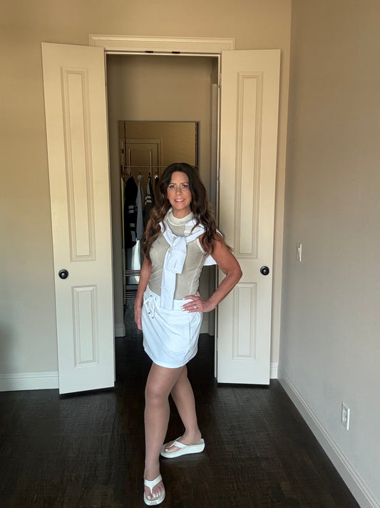 Woman standing in a room with open doors, wearing a white dress and beige cardigan.