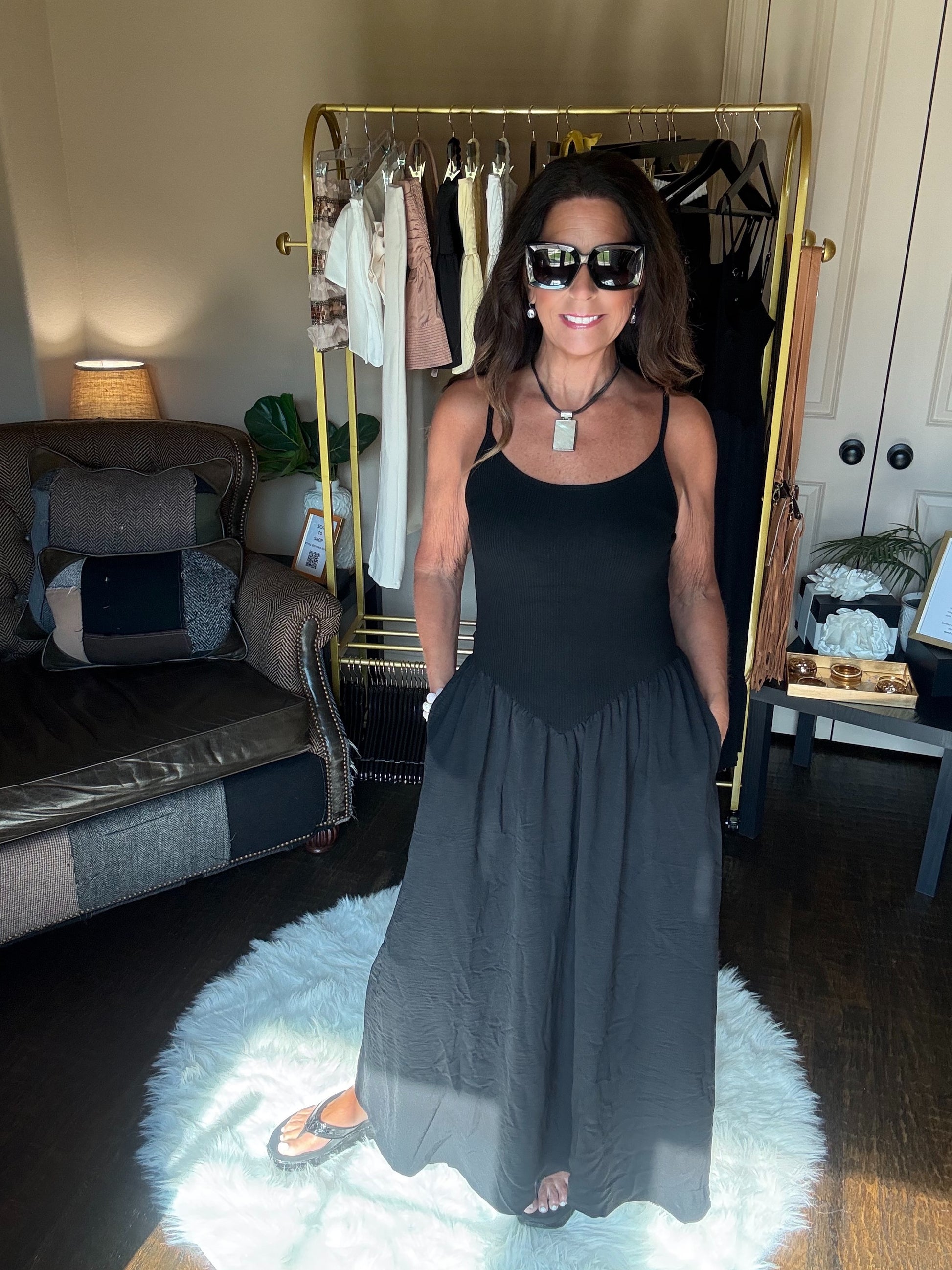 Woman wearing a black top and gray skirt standing in a room with a clothing rack and sofa.
