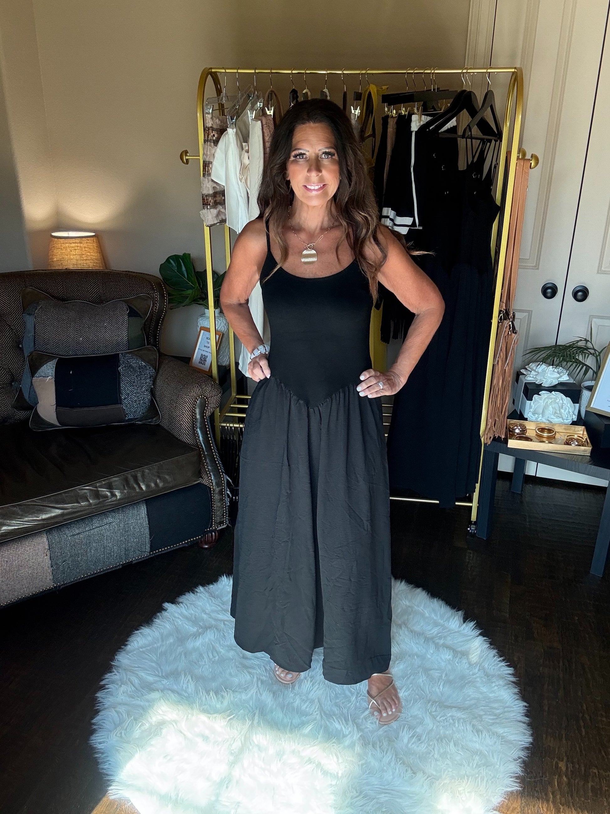Woman wearing a black dress standing in a room with a couch and clothes rack.