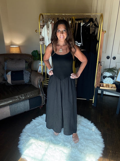 Woman wearing a black dress standing in a room with a couch and clothes rack.