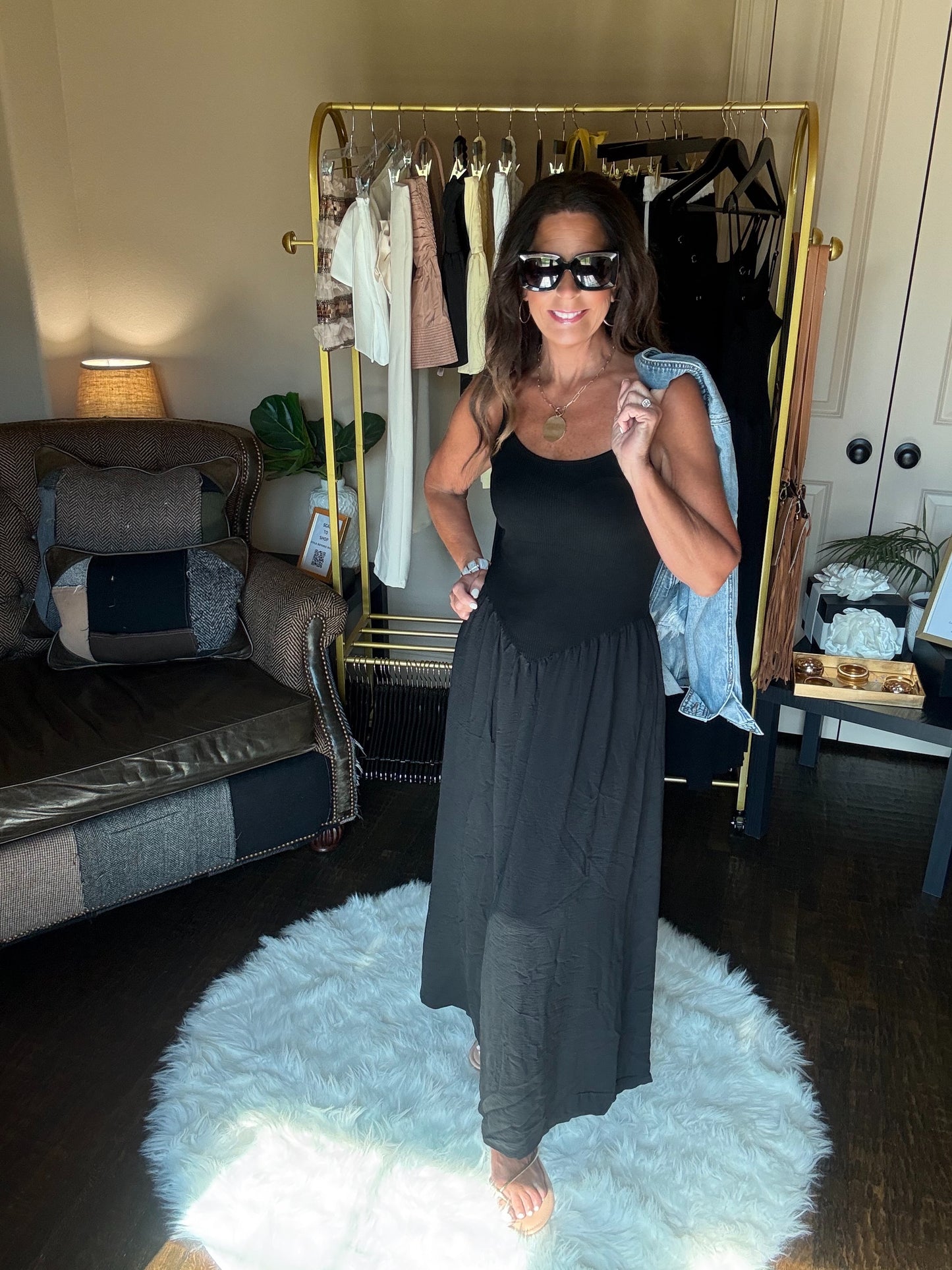 Woman in a black dress standing in a room with a coat rack and furniture.