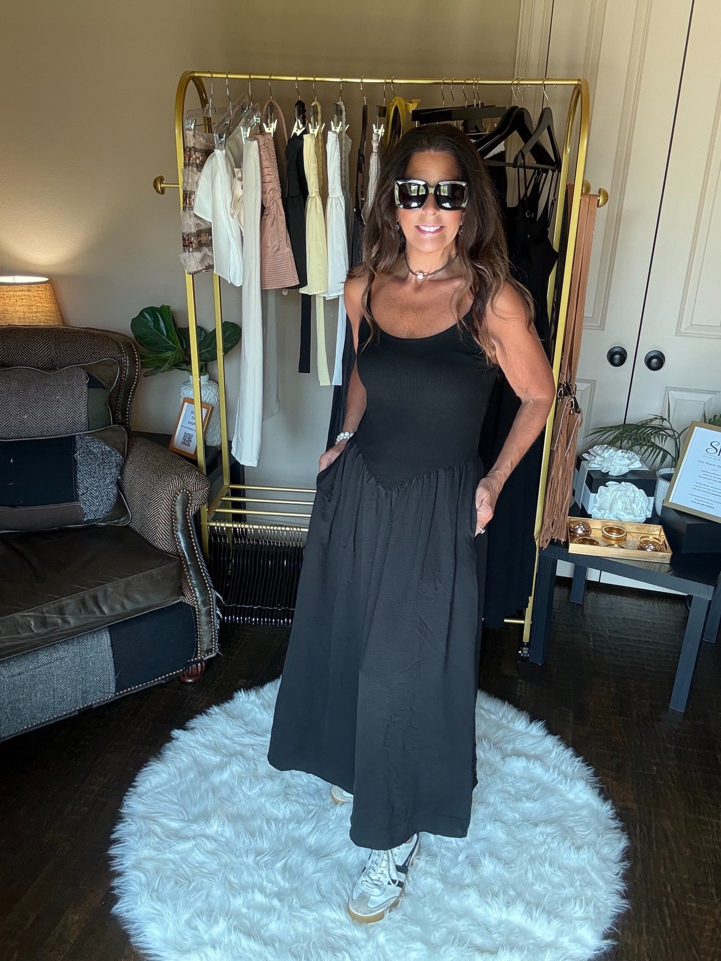 Woman in a black dress standing in a room with a clothing rack and furniture.