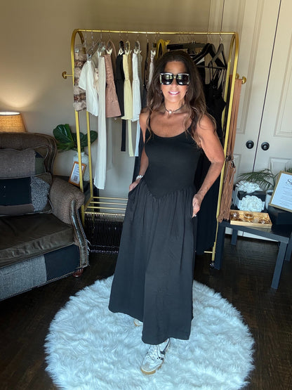 Woman in a black dress standing in a room with a clothing rack and furniture.