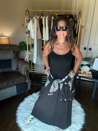 Woman in a black dress and sunglasses standing in a room with a clothing rack and furniture.