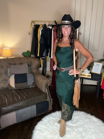 Model is wearing a hunter green satin and lace maxi dress with spaghetti straps and an asymmetrical hem and a cowboy chic vibe.