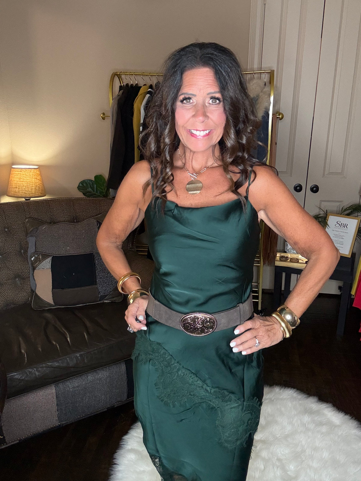 Model is wearing a hunter green satin and lace maxi dress with spaghetti straps and an asymmetrical hem and a cowboy chic vibe.