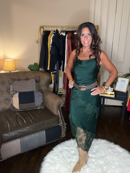 Model is wearing a hunter green satin and lace maxi dress with spaghetti straps and an asymmetrical hem and a cowboy chic vibe.