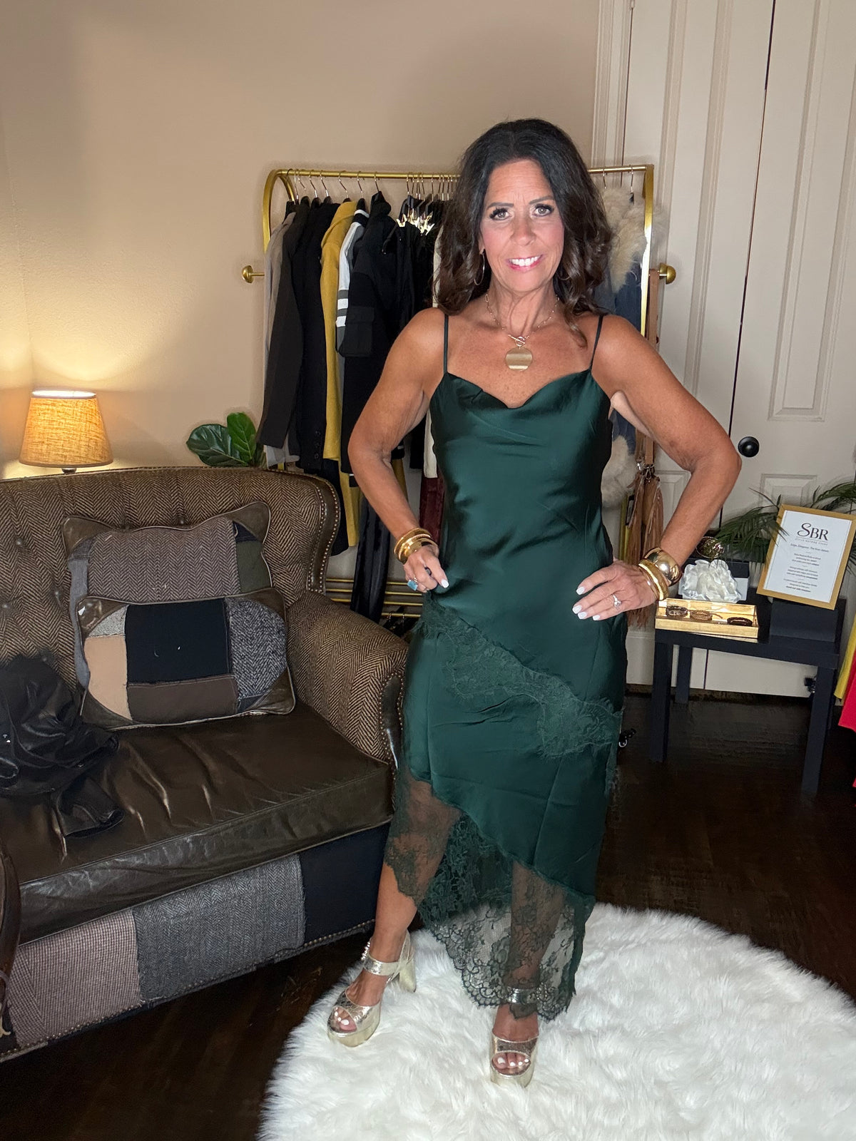 Model is wearing a hunter green satin and lace maxi dress with spaghetti straps and an asymmetrical hem.