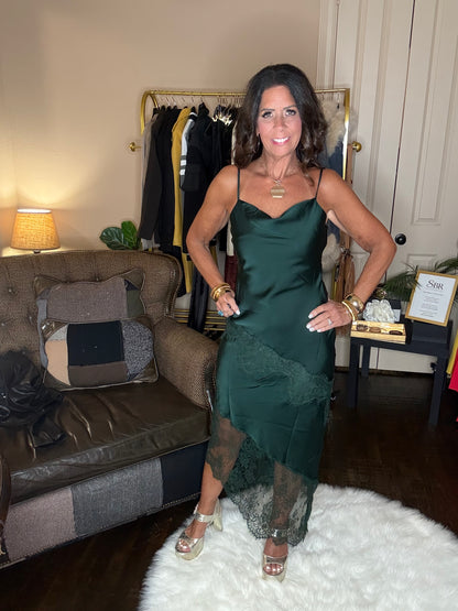 Model is wearing a hunter green satin and lace maxi dress with spaghetti straps and an asymmetrical hem.