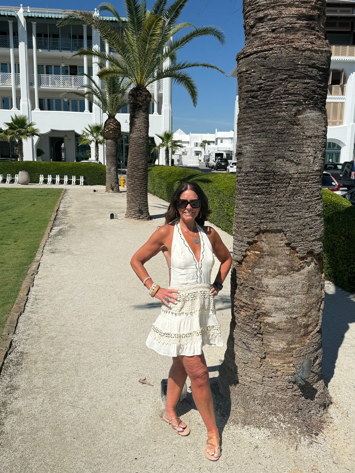 woman posing by a palm tree wearing a cream and gold halter dress