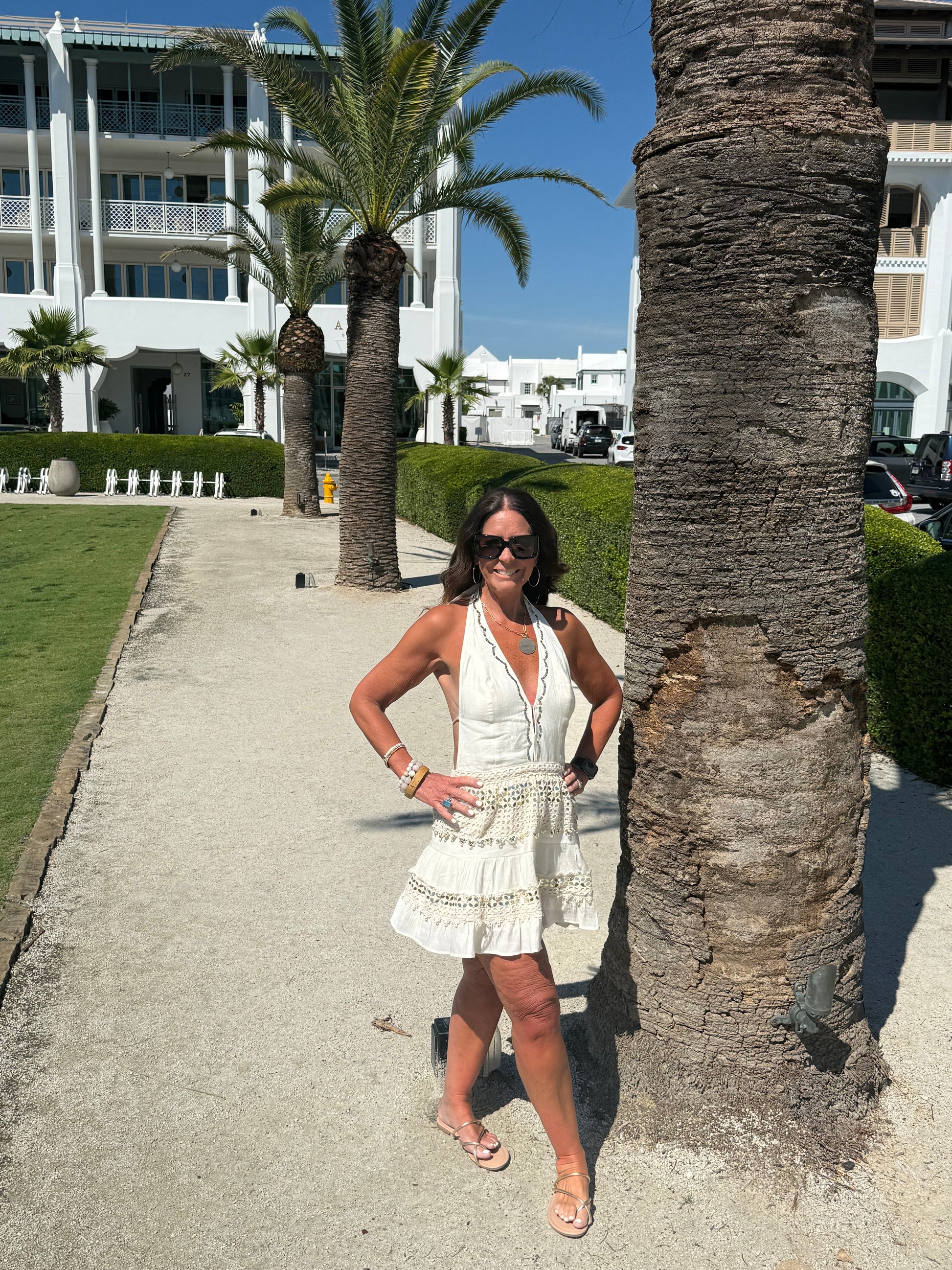 woman posing by a palm tree wearing a cream and gold halter dress