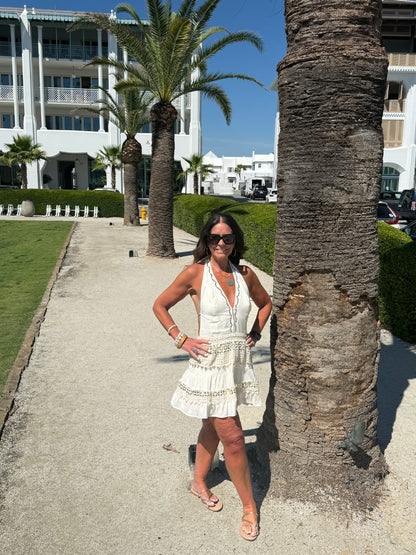 woman posing by a palm tree wearing a cream and gold halter dress