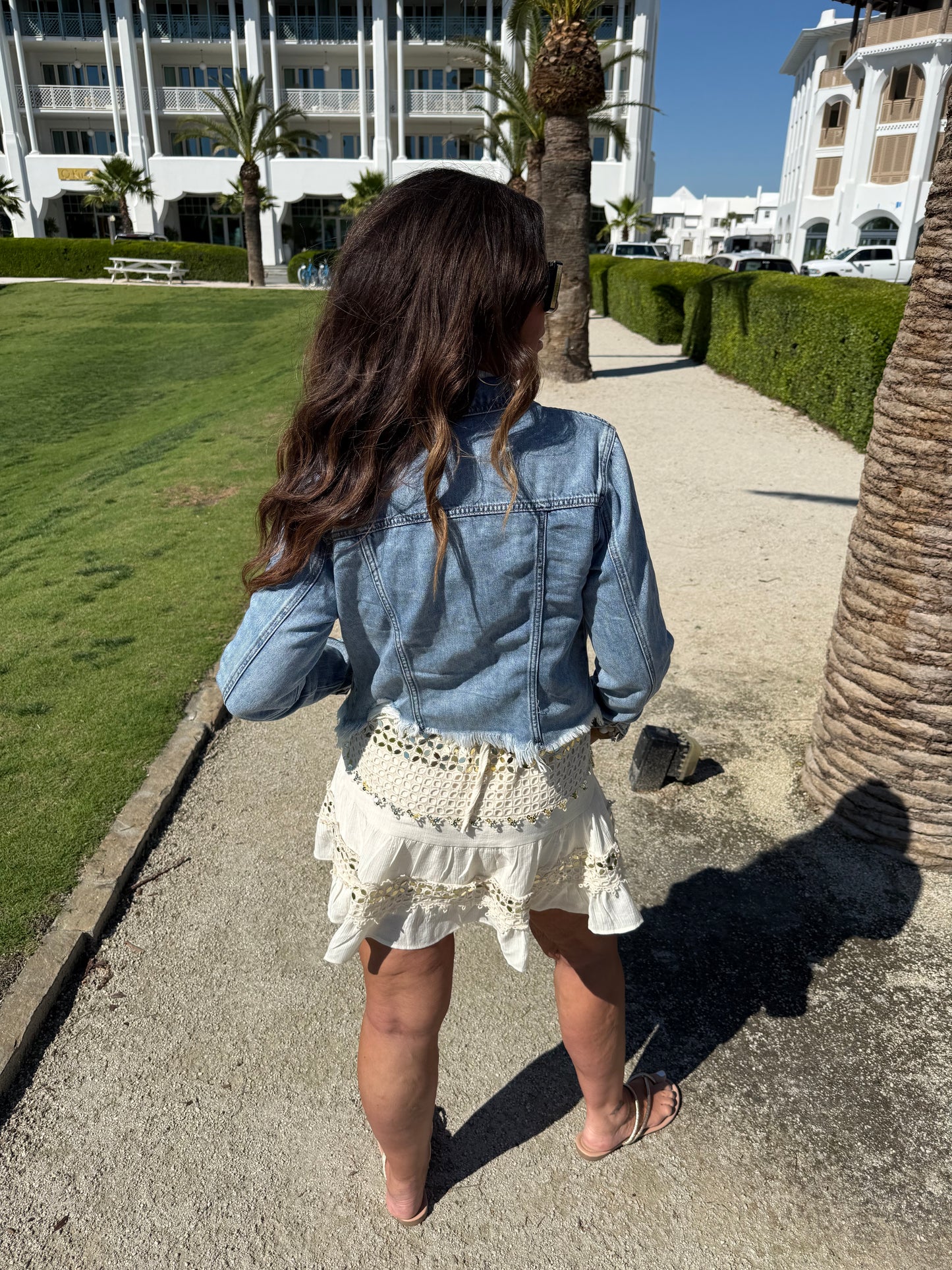 woman showing back of cream and gold dress layered with a cropped jean jacket