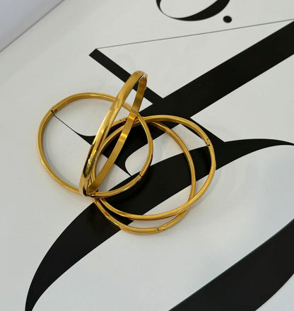 four thin gold bracelets in a random scattered display on a black and white table