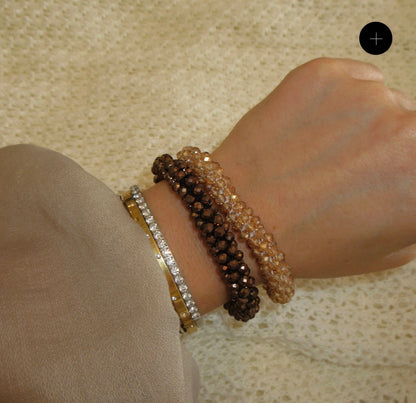 a woman's wrist wearing four different beaded bracelets amber, brown, diamond, gold