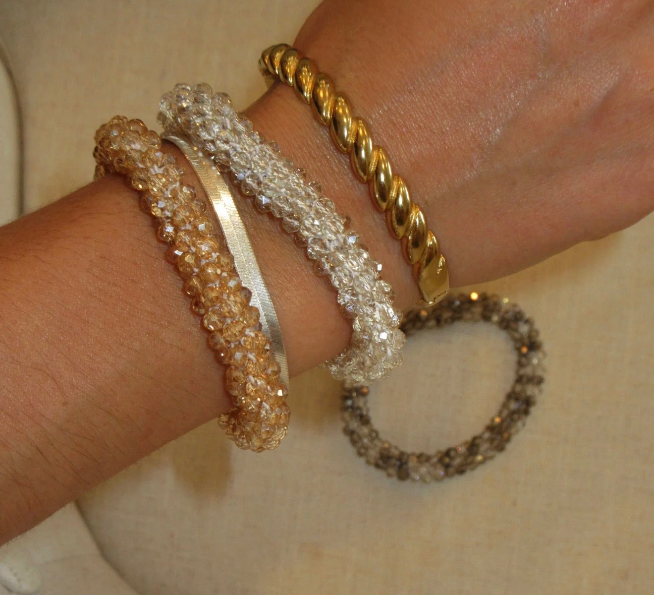 Three gold bracelets on a wrist against a neutral background