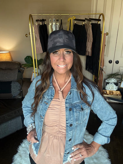 Woman wearing a denim jacket and black cap indoors with a mirror and clothing rack in the background.