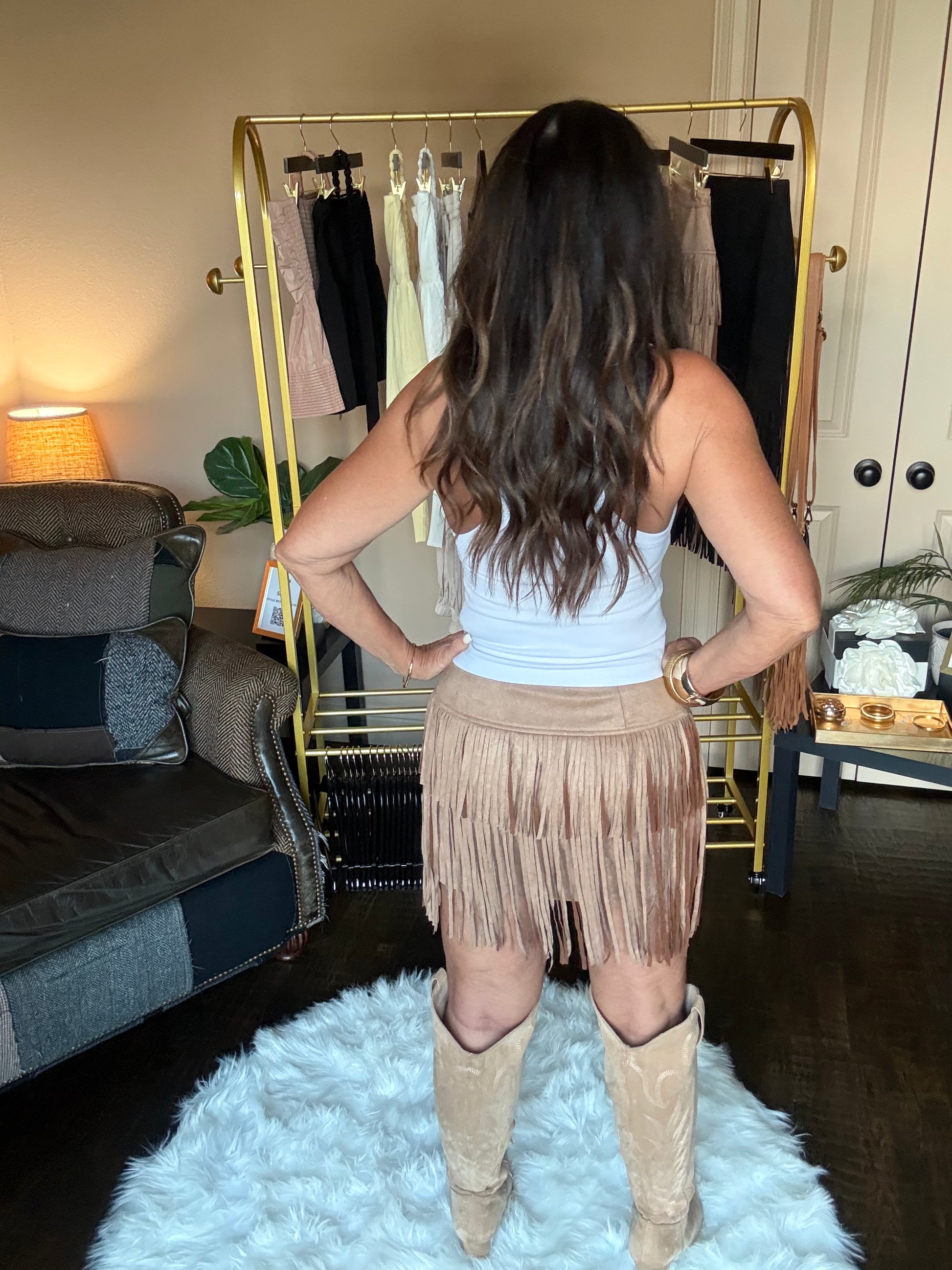 Woman modeling a tan mini skirt with fringe in a home boutique.