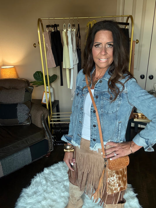 Woman holding a brown fringe handbag in a room with clothing racks and a lamp.