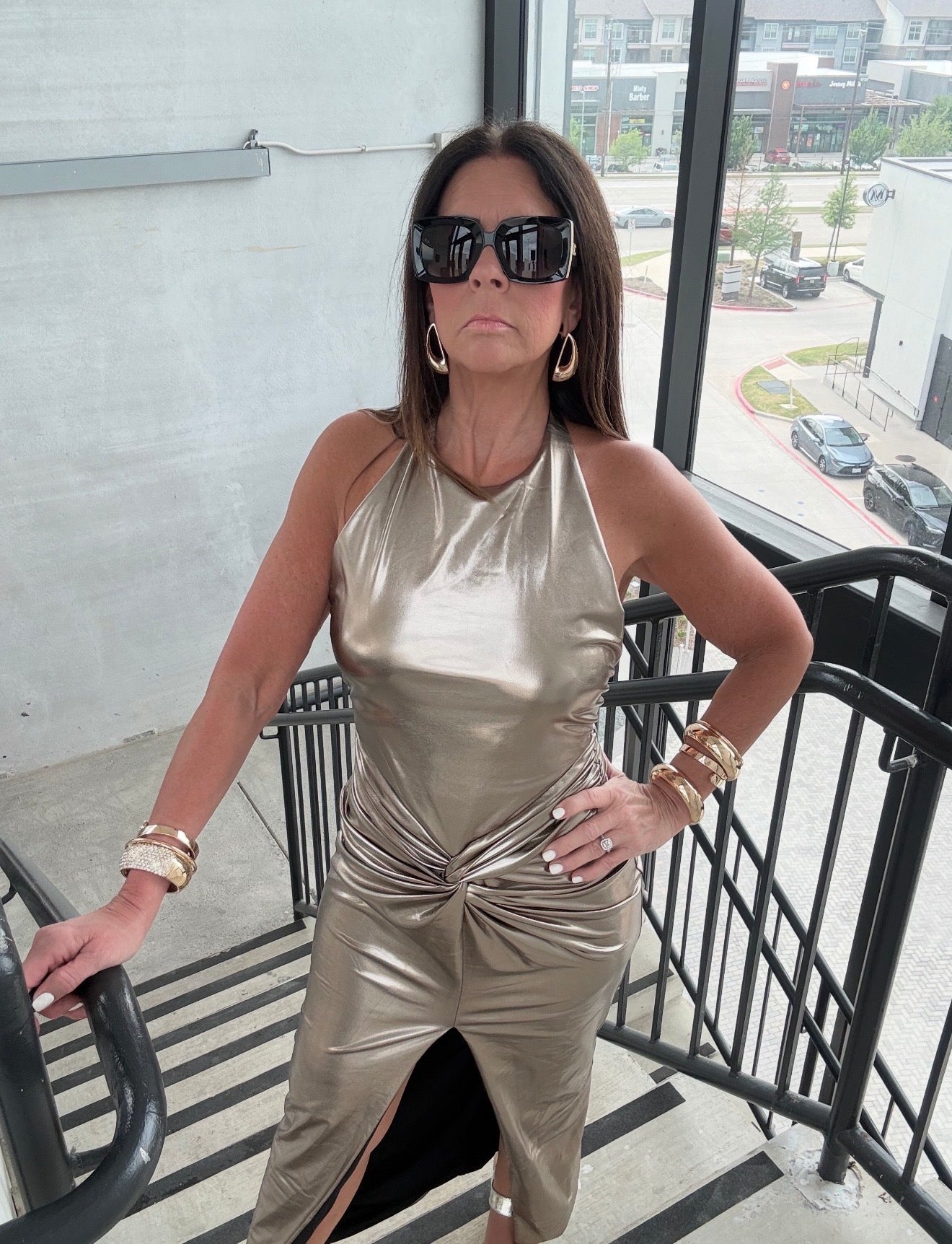 Woman in a gold metallic dress standing on a balcony with a cityscape background