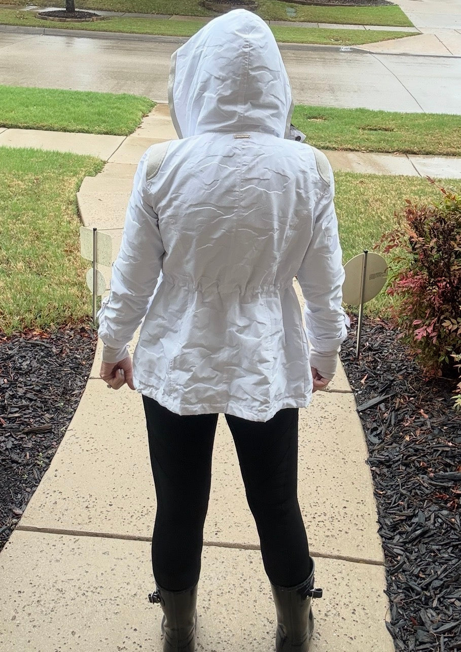 Person wearing a white raincoat walking on a sidewalk.