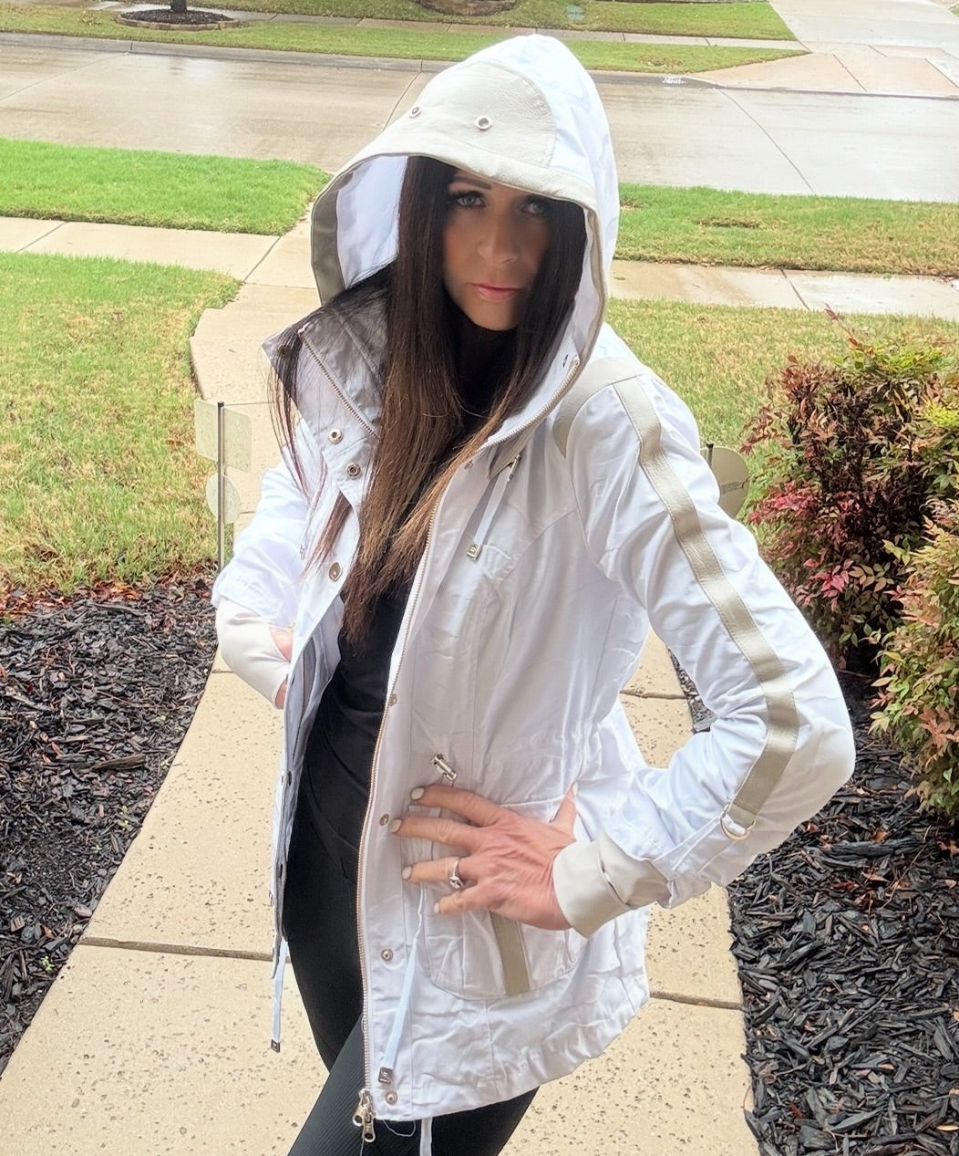 Woman wearing a white raincoat with transparent panels on a sidewalk.