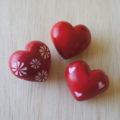Three red heart-shaped objects with floral and polka dot patterns on a light wooden surface.