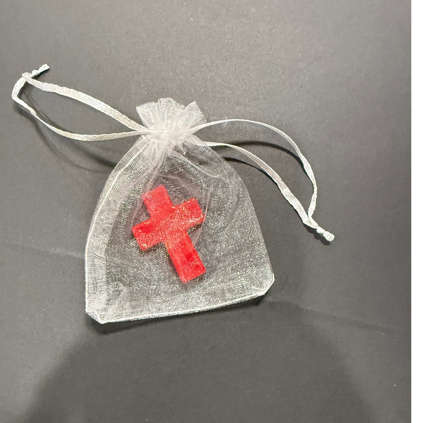 Red cross charm in a clear organdy bag on a dark surface