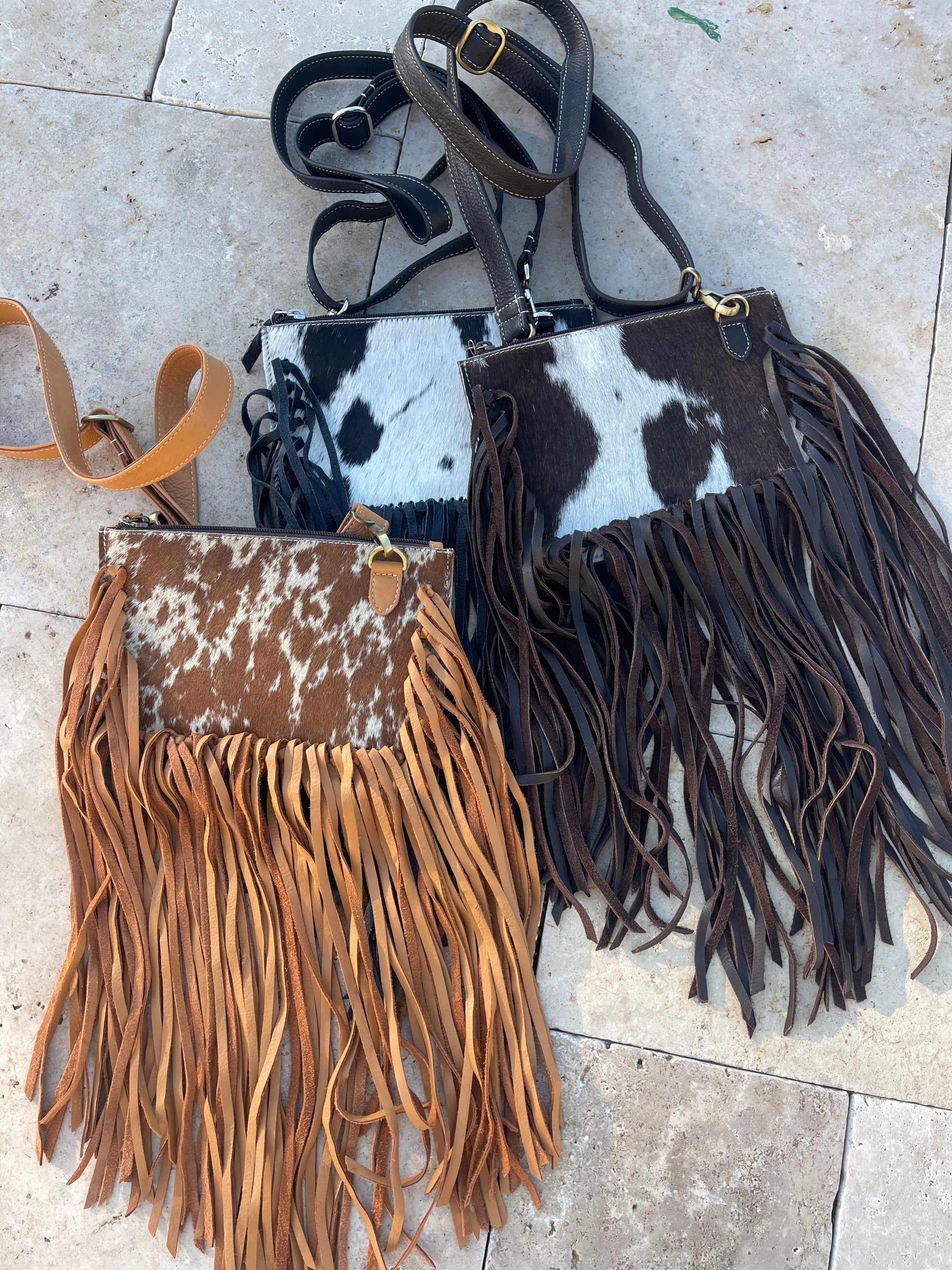 Two leather handbags with fringe details on a tiled floor.