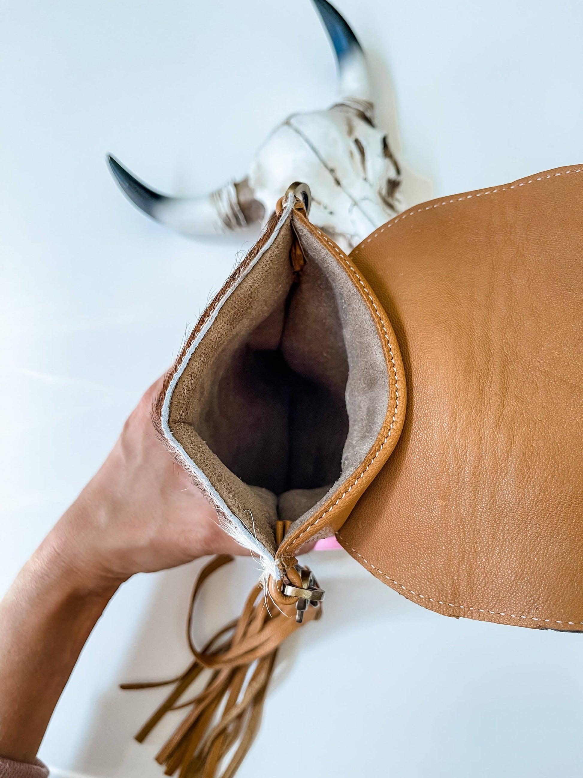 Brown leather bag with tassel held by a hand on a white background