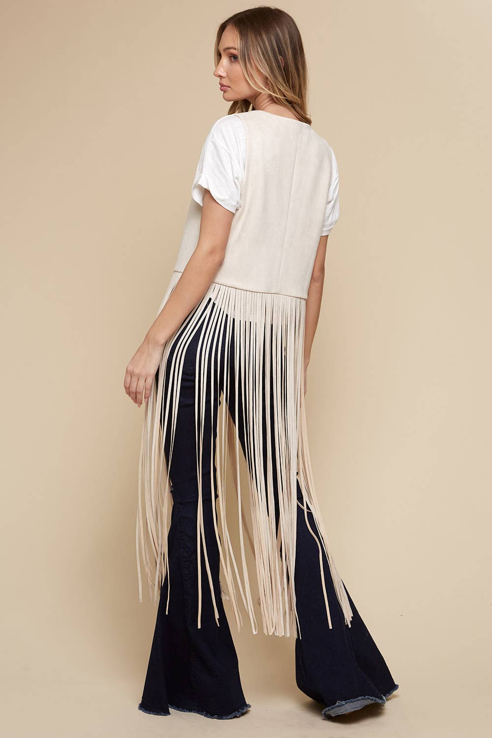 Woman wearing a white fringe top and black pants on a beige background