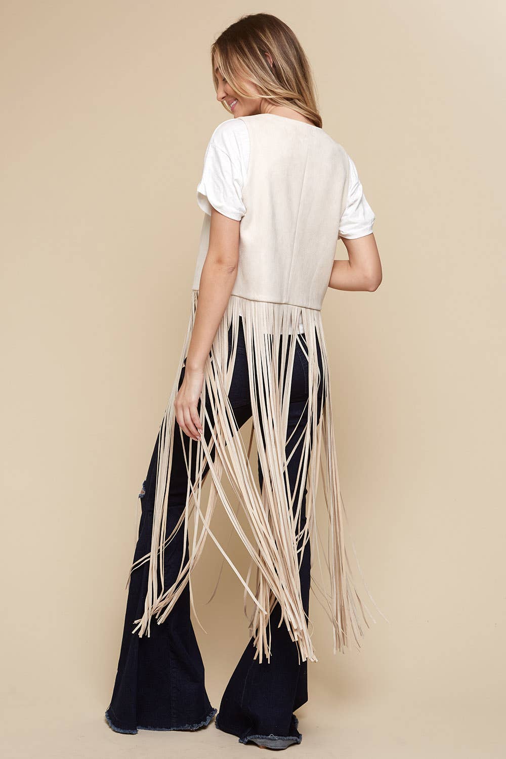 Person wearing a white top and black pants with fringe details on a beige background
