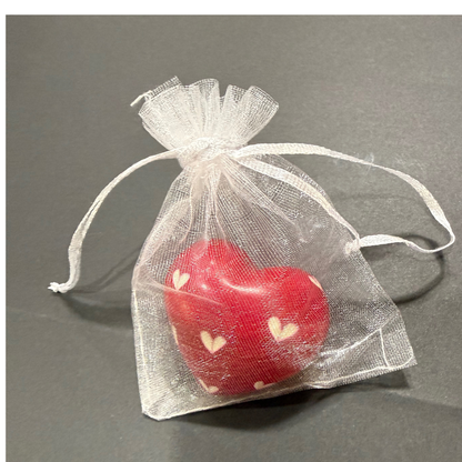 Red heart-shaped object with white hearts in a clear organza bag on a gray background